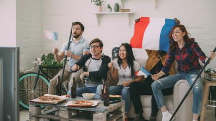 Group of young friends sports fans with French national flags watching sport championship on TV...