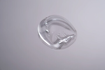 Drop of cosmetic transparent gel on a grey background. The texture of the serum, heir gel or hyaluronic booster.