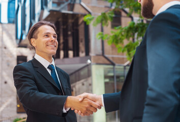 Confident businessman and his colleague in front of modern office building. Financial investors in formal wear are talking outdoor. Banking and business.