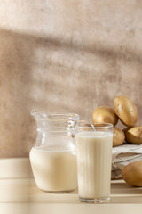 A glass and a jug of potato milk with raw potatoes in a bowl. 