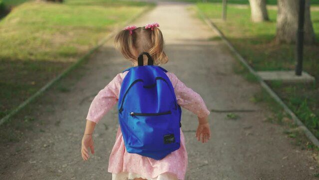 back to school. a little girl with a backpack runs through the green park to school along the path. education kid dream concept. a small child with a backpack back view runs sun the park to school