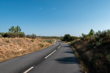 Estrada asfaltada com os traços tracejados a meio de um campo com uma curva à frente numa manhã...