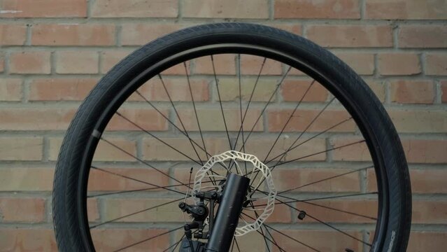Black bicycle wheel rotates against red brick wall background. Bike service and care concept