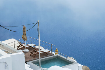 Fototapeta na wymiar Two sun beds next to a small pool and a stunning view of the foggy Aegean Sea in Santorini