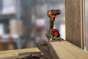A black cordless screwdriver stands on a wooden table. Free space for your products. The interior of the repair shop.