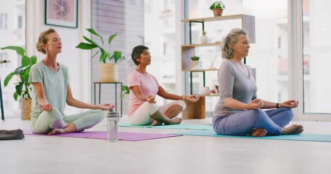 Mature women meditating in lotus pose with mudra hand gesture during a fitness class in a yoga studio. Calm, relaxed and focused ladies sitting and praying quietly for inner peace and zen energy