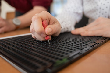 A woman uses a special stencil and stylus to write a letter in braille. 