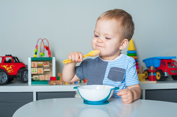 Toddler boy eats with spoon and is covered in food. Baby food, food allergies, self-feeding....