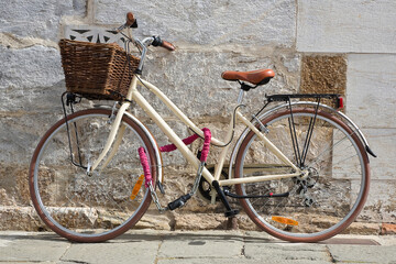 Fototapeta na wymiar Women's bicycle with basket closed with chain against a wall in a italian street paved of stone