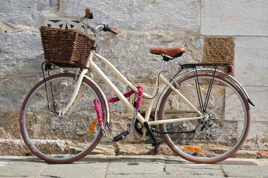 Women's bicycle with basket closed with chain against a wall in a italian street paved of stone
