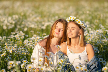 Naklejka na ściany i meble Two girls enjoying a summer day in a field of daisies. Girlfriends hugging and laughing in nature. A same-sex couple happily walking outdoors.