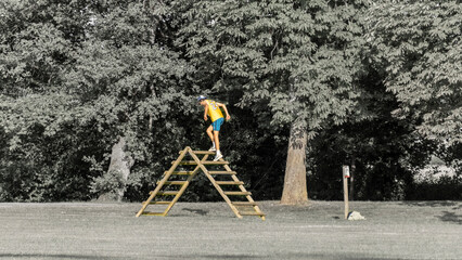 Young man from behind climbing a wooden obstacle in a green park