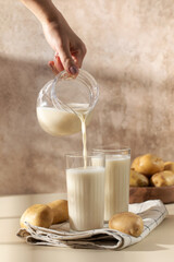 Potato milk is poured into a glass from a jug. Lactose-free milk.