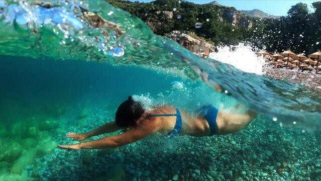 Slow-motion half underwater video at the border of air and water. Beautiful girl dives into the sea of the Montenegro coast.