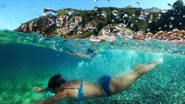 Slow-motion half underwater video at the border of air and water. Beautiful girl dives into the sea of the Montenegro coast.