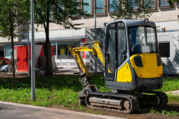 A small yellow excavator at a construction site in the city.