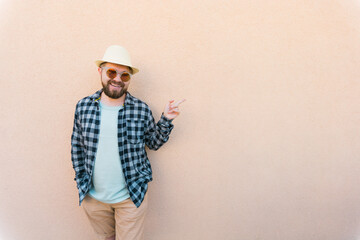 Bearded man in summer clothes and hat pointing on beige wall on street city urban and travel concept - copy space and empty space for advertising
