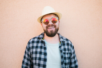 Bearded man portrait in summer clothes and hat stand over beige wall on street city urban and travel concept