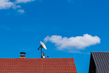 Satellite dishes on a tiled roof of a residential building.