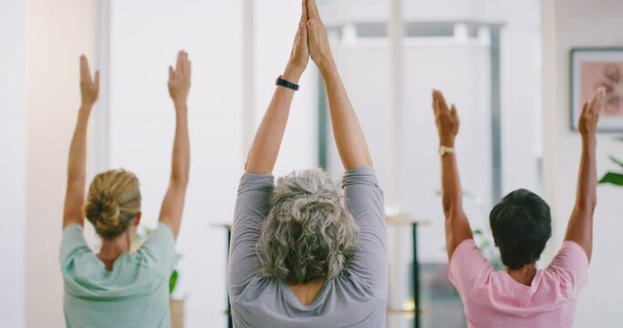 Diverse group of yogis sitting together and finding inner mental balance or peace. Practicing calming breathing exercises. Mature women meditating with prayer hand above head in zen yoga studio class