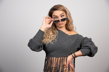 Young blonde woman playing with eyeglasses on gray background