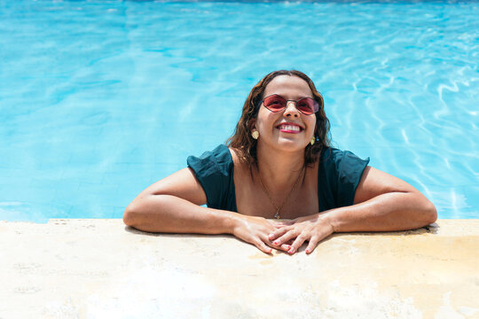 Latin woman with sunglasses relaxing by the summer pool