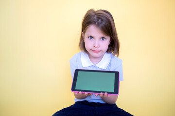 Pretty girl schoolgirl teenager student holding digital tablet showing blank screen with place advertising mockup isolated on yellow background