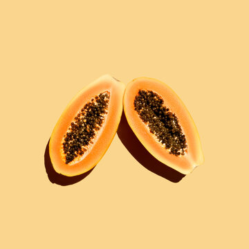 two ripe papaya halves with seeds on orange background