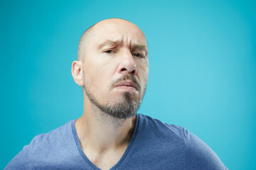 Obraz premium Close up of unhappy bald man in blue shirt on blue wall background.
