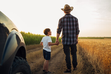 father and son holding hands walking in farmland