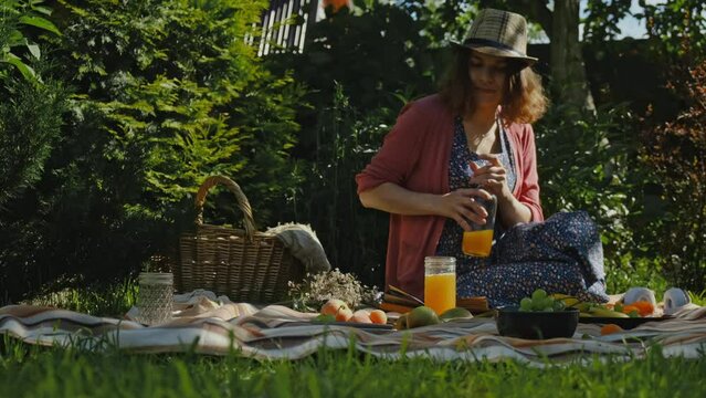 Young woman having summer picnic. Girl drinking juice eating outside. Summer outdoors activities. Backyard picnic.