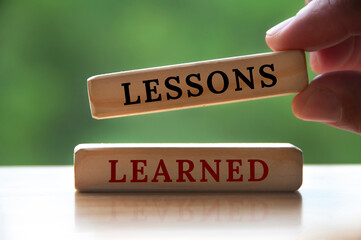 Lessons learned text on wooden blocks with hand holding and blurred nature background. Learning...