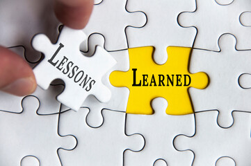Lessons learned text on Jigsaw Puzzle with one hand holding a missing jigsaw pieces. Improvement...