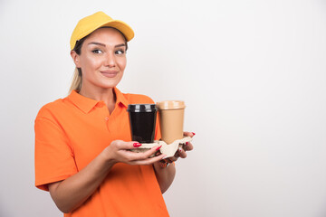 Blonde female courier holding two cups of coffees looking sideways on white background