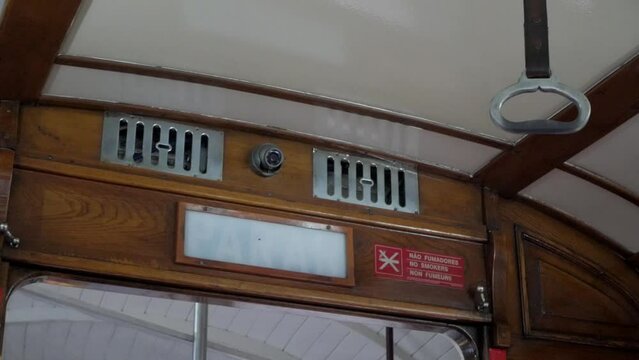 Lisbon historical cable tram next stop announcement sign flashing. Vintage transportation vehicle wooden interior. Safety handle for commuters. CCTV security camera and ventilation grills above sign.
