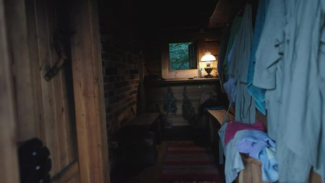 Dark Traditional Wooden Sauna Spa Cabin Room, Relaxing Room, Wooden Bench and Hanging Towels along the Brick Wall, Lamp and Window at the Back
