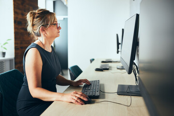 Concerned businesswoman working on computer in office. Busy woman sitting at desk at front of computer monitor. Focusing on work. Open office. Copy space right