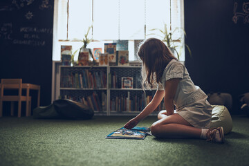 Child solving riddle in book in school library. Primary school pupil is involved in book with...