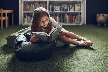 Schoolgirl reading book in school library. Primary school pupil is involved in book. Child doing...