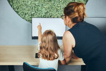 Teacher assisting schoolgirl while computer class at primary school. Child using computer on elementary computer science class. Teacher helping to find task solution. Giving clues. Back to school