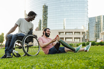 Happy diverse friends with physical disability having fun using mobile phone outdoor - Focus on leg...
