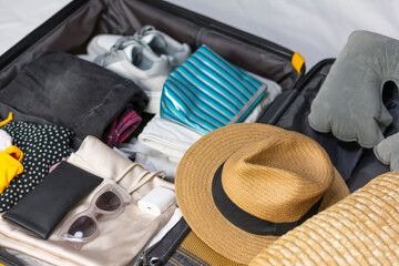 Top view flat lay suitcase with neatly folded clothes with straw hat and bag and inflatable pillow and sneakers. Concept: travel, tourism, clothing accessories, vacation 