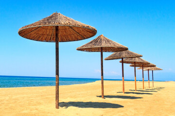 Row of wooden umbrellas at sandy beach, sea and blue sky vacation background, Greece