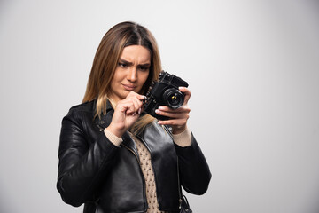 Girl in leather jacket checking photo history on camera and looks dissatisfied