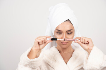 Young woman in a bathrobe opening a lipstick