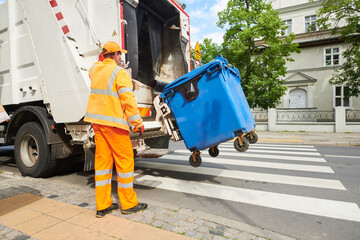 garbage and waste removal services. Worker loading waste bin into truck at city - 515608286