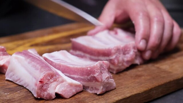 The chef cuts pork ribs into pieces. Divides  raw pork ribs with a knife on a wooden board. Preparation food concept