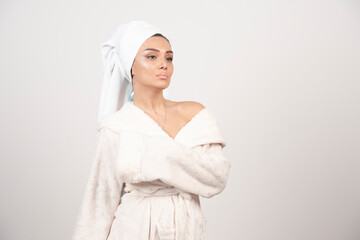 Beautiful young woman in a white bathrobe posing on a white wall