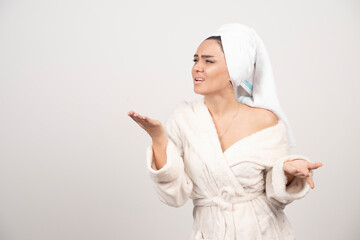 Beautiful young woman in a white bathrobe posing on a white wall