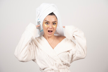 Young woman in bathrobe and cosmetic eye patches posing